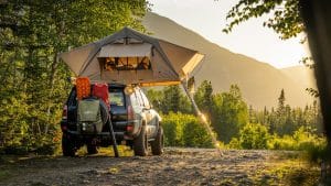 man in green jacket sitting on black and yellow camping chair near tent during daytime